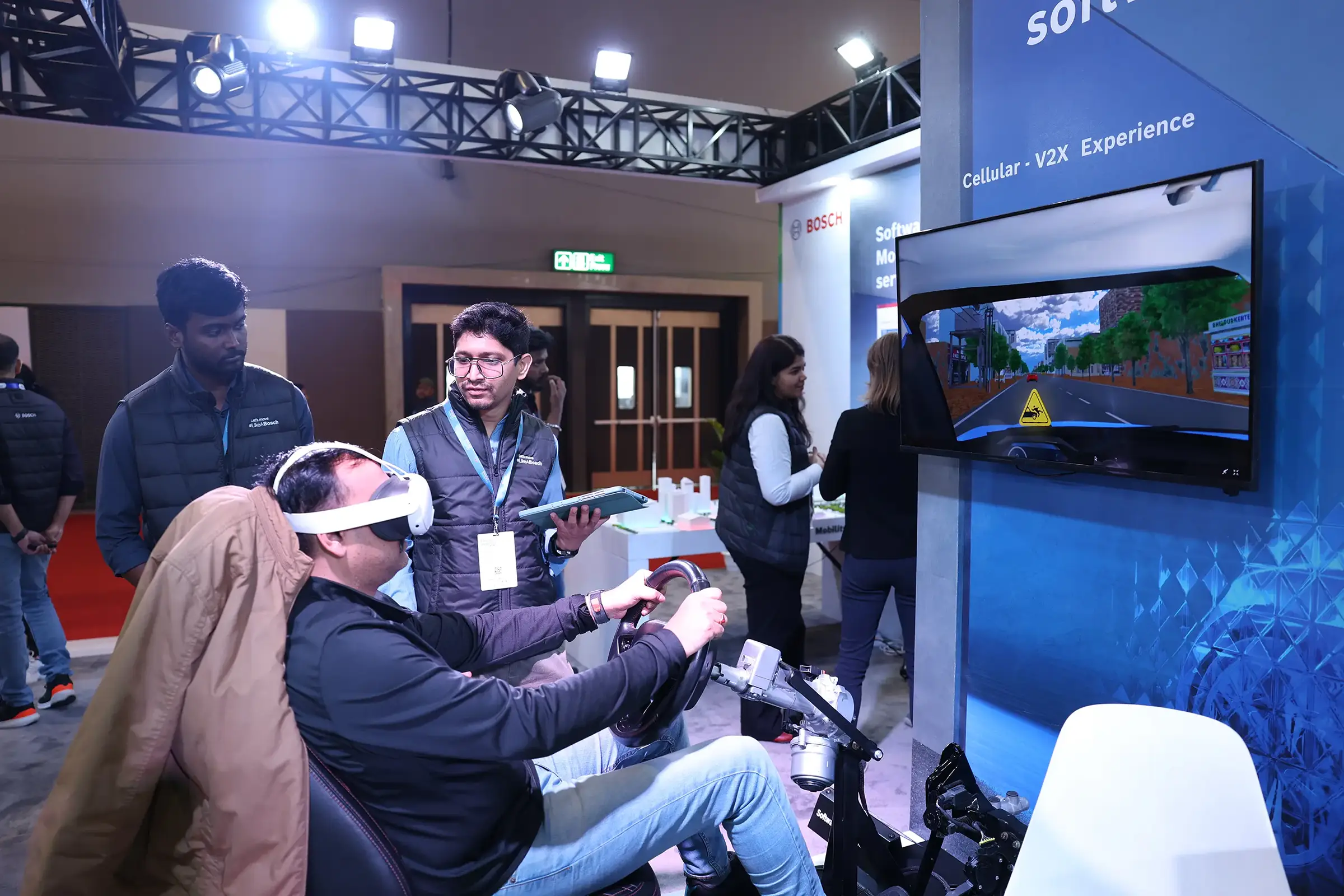 A man experiences a V2X experience using a VR headset and steering wheel at the Bosch booth.